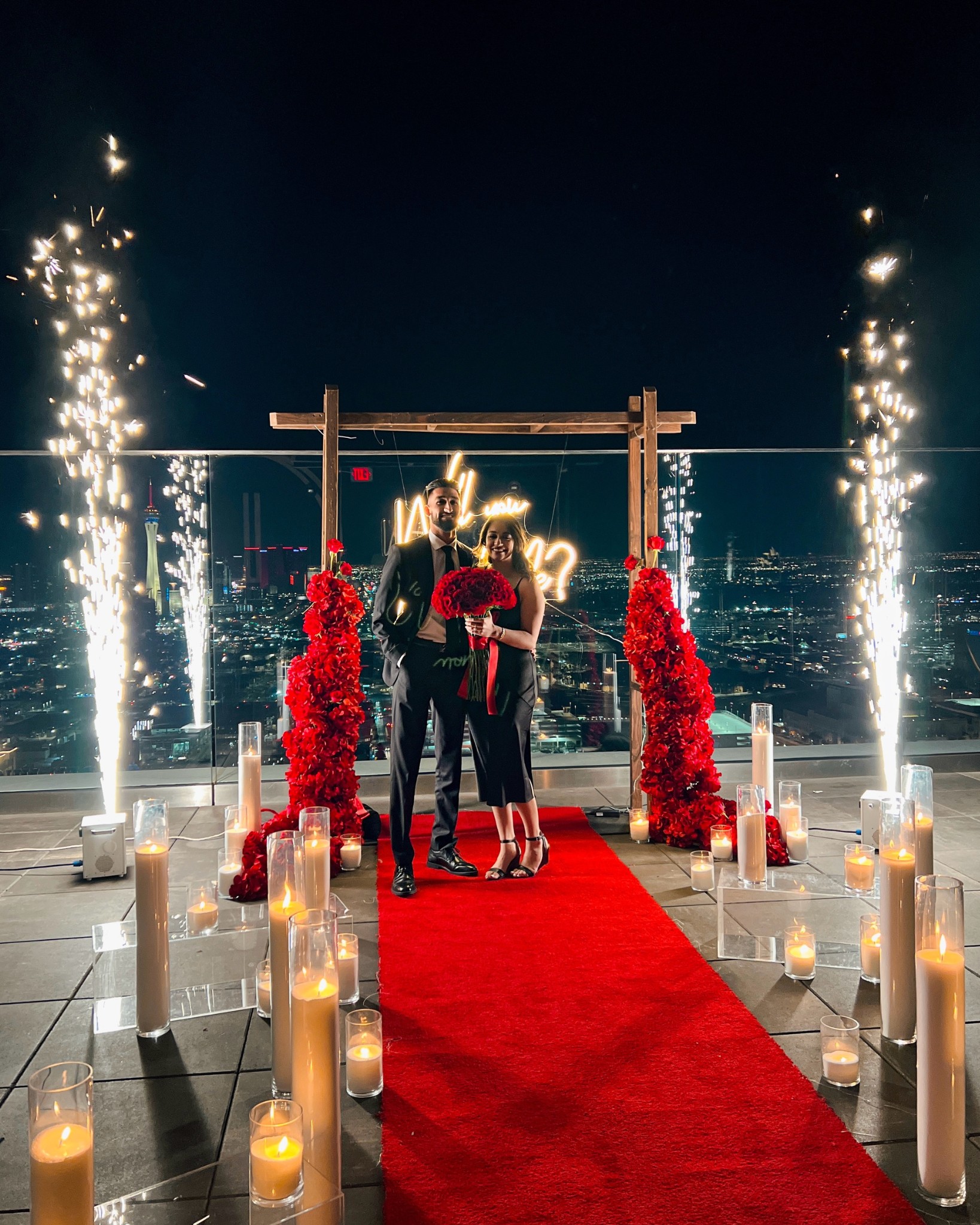 outdoor wedding proposal las vegas strip view rooftop balcony with sparkler fountain and neon will you marry me sign and red carpet candles and flowers